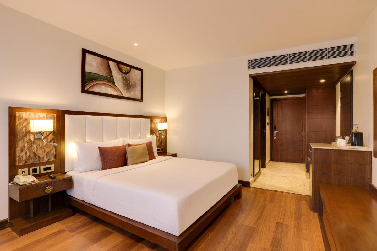 a bedroom with a large white bed and a bathroom at Saura Hotel, Agra - A Club Mahindra Associate in Agra