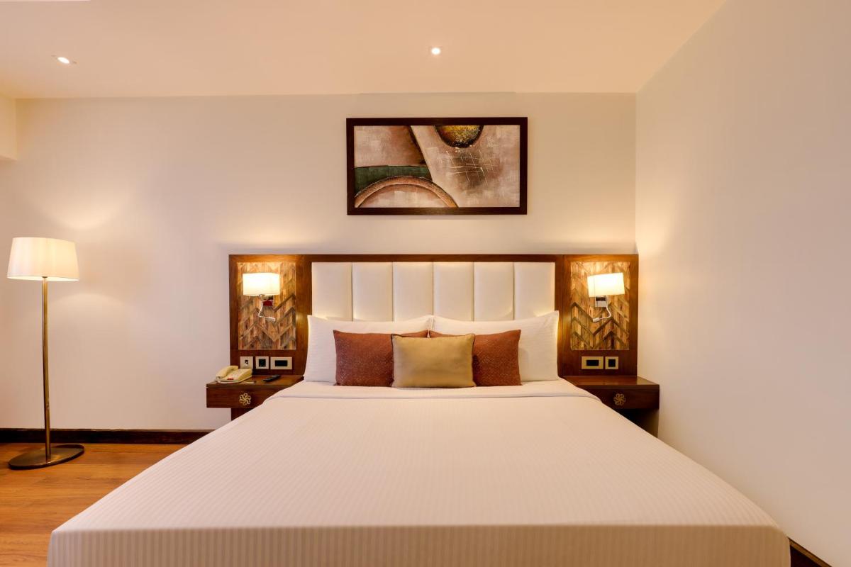 a bedroom with a large white bed and two lamps at Saura Hotel, Agra - A Club Mahindra Associate in Agra