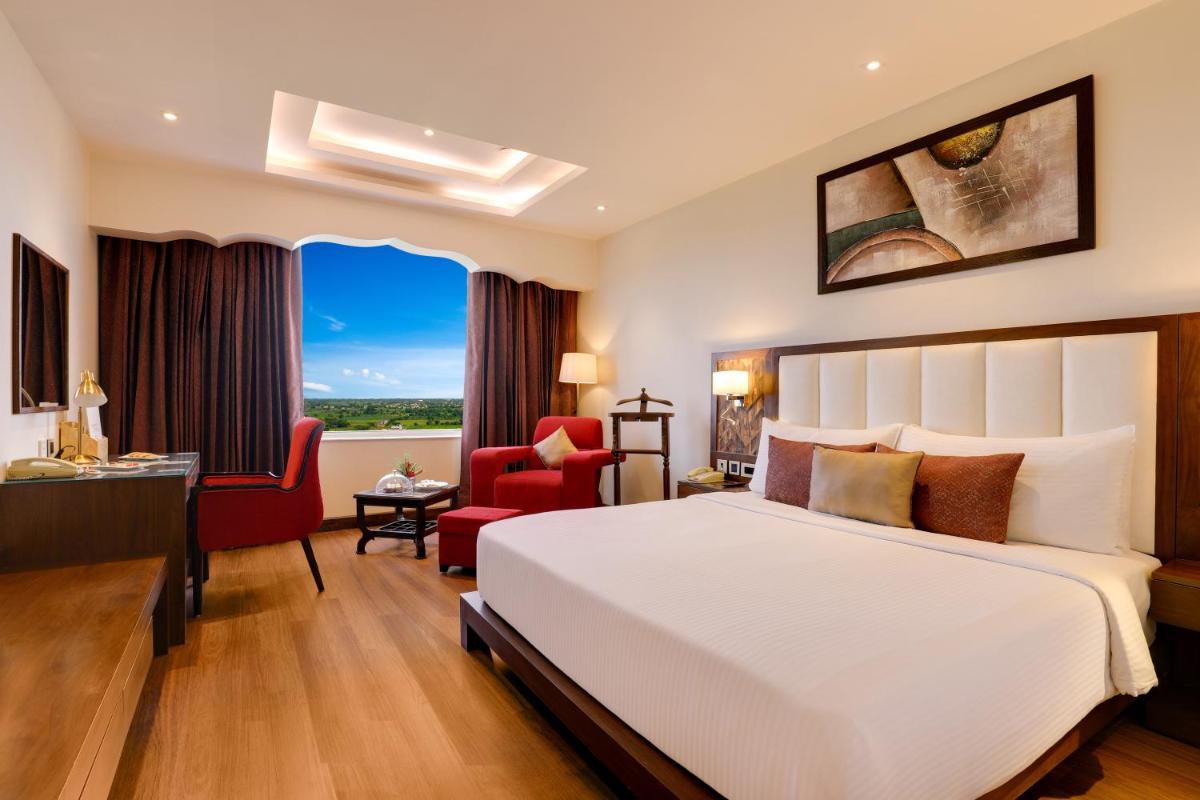 a bedroom with a white bed and a red chair at Saura Hotel, Agra - A Club Mahindra Associate in Agra