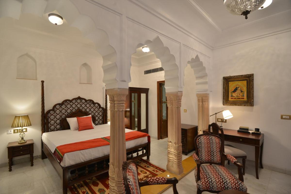 a bedroom with a bed and a desk and chairs at Haveli Dharampura & Golden Haveli- UNESCO awarded Boutique Heritage Hotel in New Delhi a bedroom with a bed and a desk and chairs at Haveli Dharampura & Golden Haveli- UNESCO awarded Boutique Heritage Hotel in New Delhi
