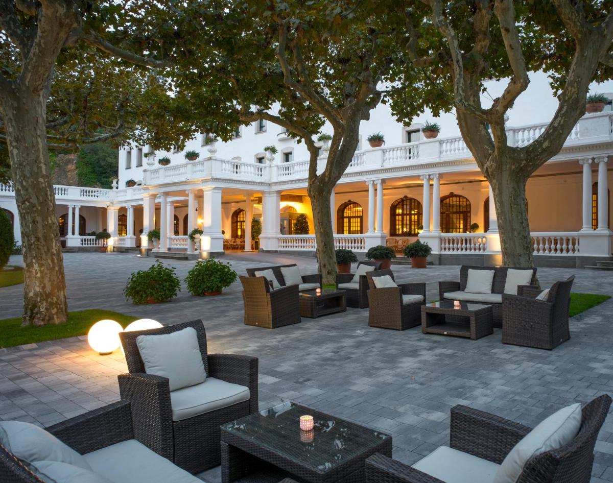 un patio al aire libre con sillas y mesas frente a un edificio en Hotel Balneari Termes Orion, en Santa Coloma de Farners