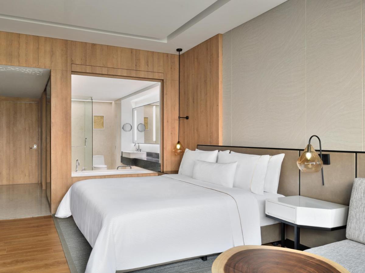 a bedroom with a large white bed and a chair at The Westin Mumbai Powai Lake in Mumbai