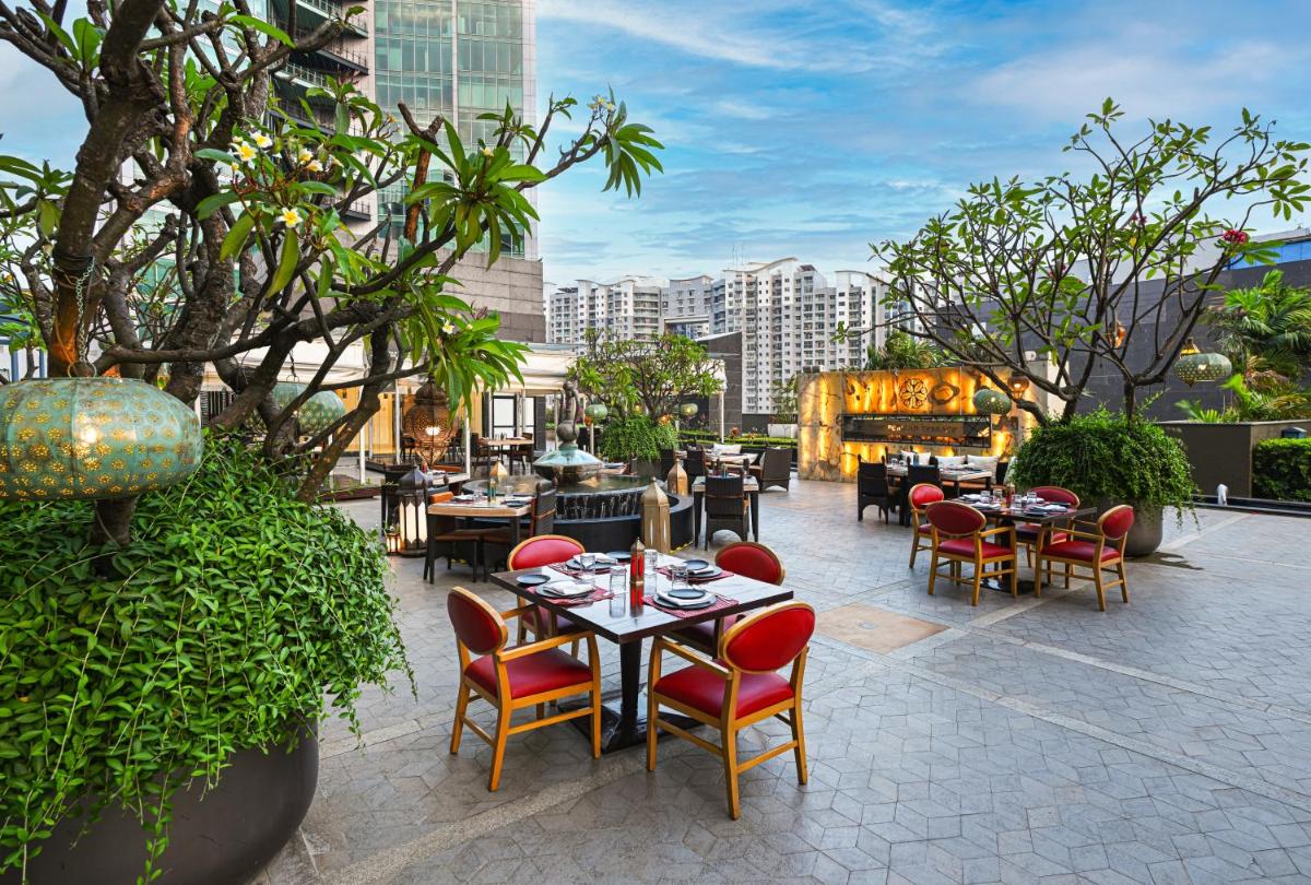 a patio with tables and chairs and trees and buildings at Sheraton Grand Bangalore Hotel at Brigade Gateway in Bengaluru