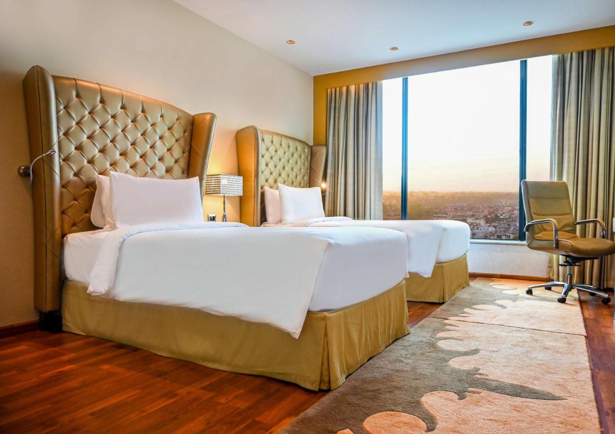 a hotel room with two beds and a large window at Radisson Blu Hotel New Delhi Paschim Vihar in New Delhi a hotel room with two beds and a large window at Radisson Blu Hotel New Delhi Paschim Vihar in New Delhi