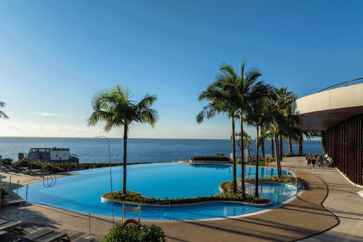 uma grande piscina com palmeiras junto ao oceano em Pestana Casino Park Hotel & Casino no Funchal