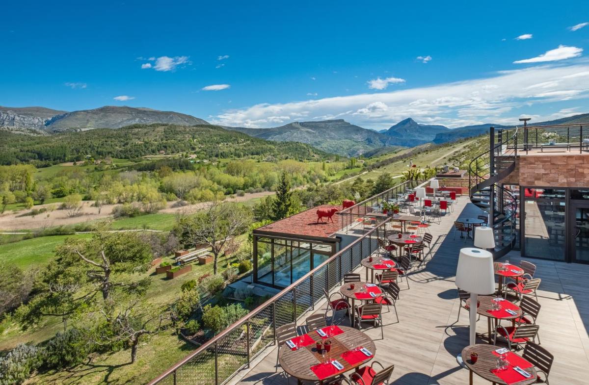une terrasse avec des tables et des chaises et des montagnes en arrière-plan dans l'établissement Hotel & Spa des Gorges du Verdon, à La Palud-sur-Verdon