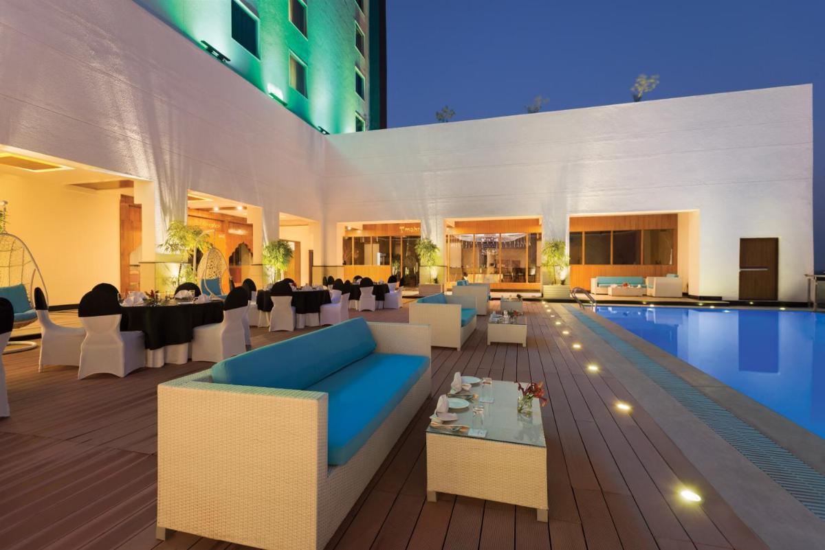 a poolside patio with a blue couch and tables at Saura Hotel, Agra - A Club Mahindra Associate in Agra