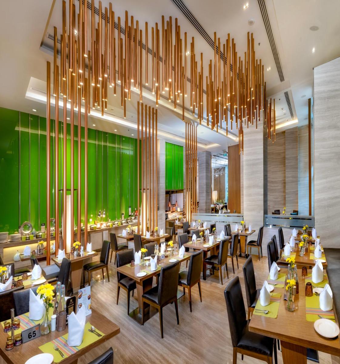 a restaurant with wooden tables and chairs and a large chandelier at Welcomhotel by ITC Hotels, Richmond Road, Bengaluru in Bengaluru