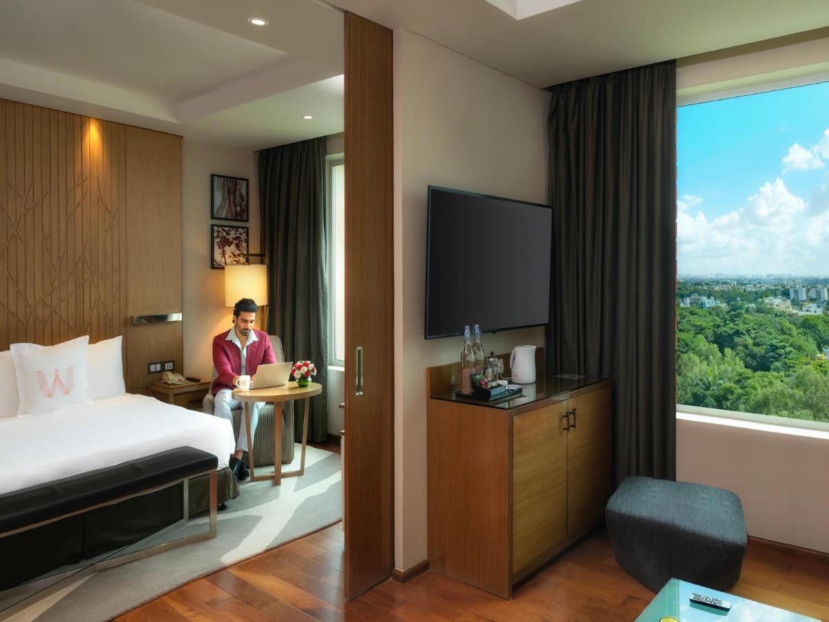 a man standing in a hotel room with a bed and a window at Welcomhotel by ITC Hotels, Richmond Road, Bengaluru in Bengaluru