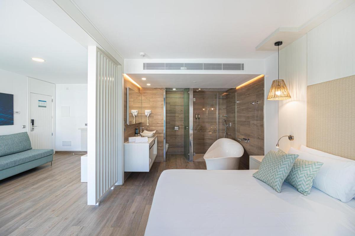 Un dormitorio con una cama blanca y un baño. en MarSenses Puerto Pollensa Hotel & Spa Adults Only, en Puerto Pollensa