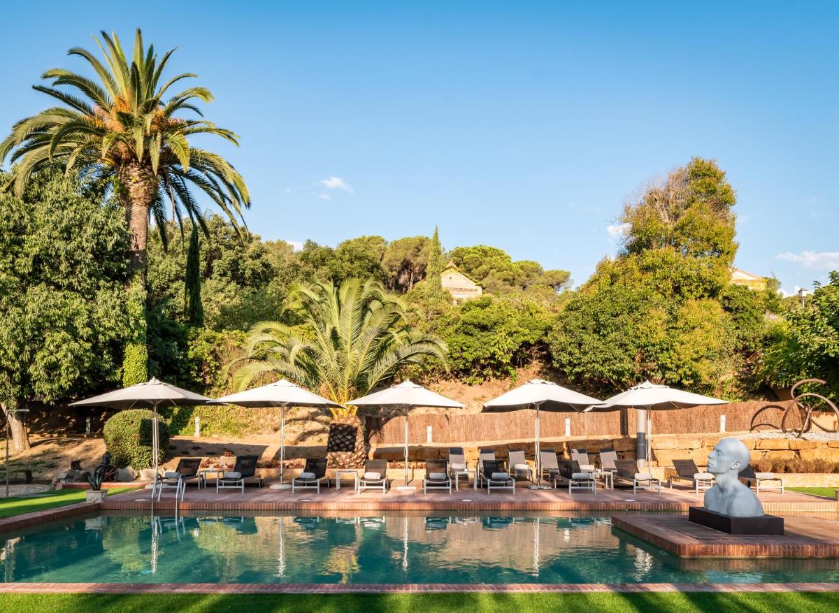 una piscina con sillas y sombrillas y una estatua en Sant Pere del Bosc Hotel & Spa - Adults Recommended, en Lloret de Mar