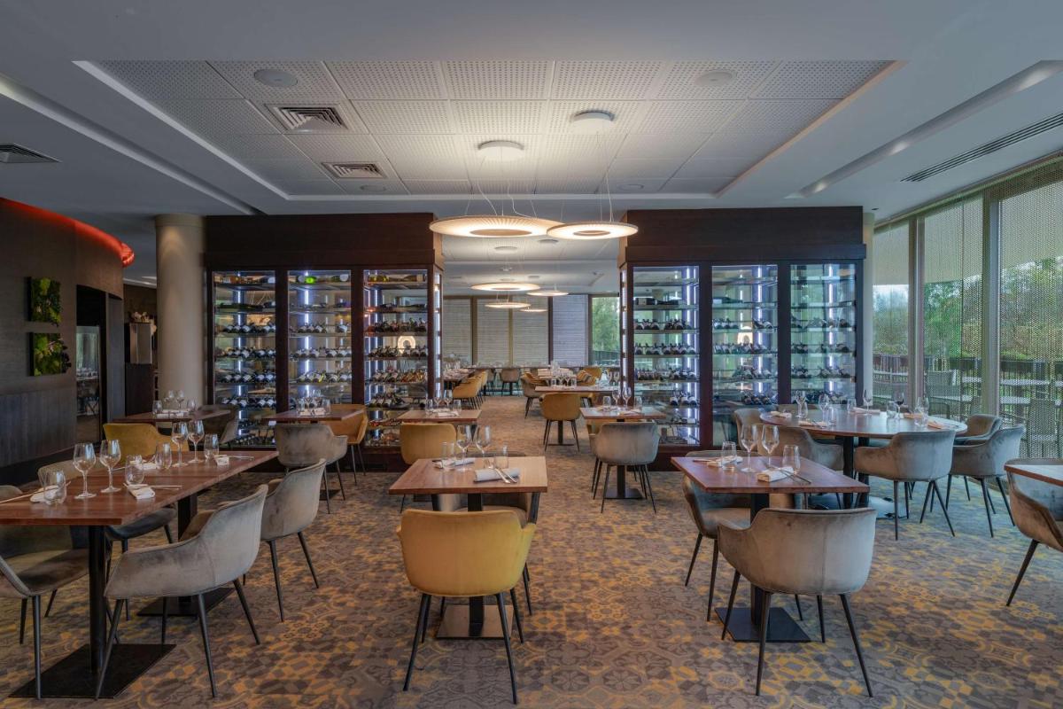 un restaurant avec des tables, des chaises et des fenêtres dans l'établissement DoubleTree by Hilton Lyon Eurexpo & Spa, à Saint-Priest