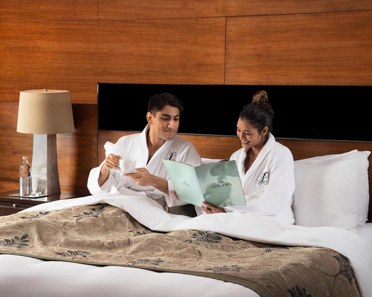 a man and a woman sitting in bed with books at The Leela Ambience Gurugram Hotel & Residences - The Luxury Urban Sanctuary in Gurgaon