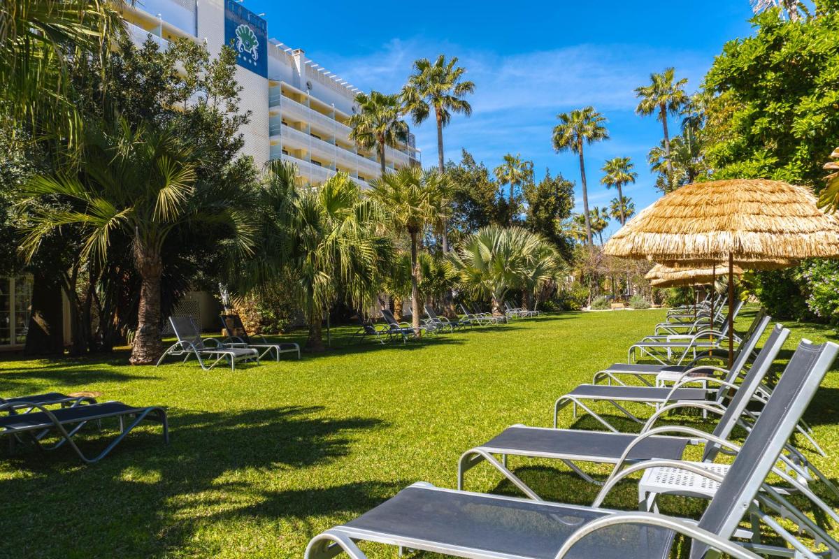 una fila de sillas de césped y sombrillas en un parque en Bahía de Alcudia Hotel & Spa, en Puerto de Alcudia