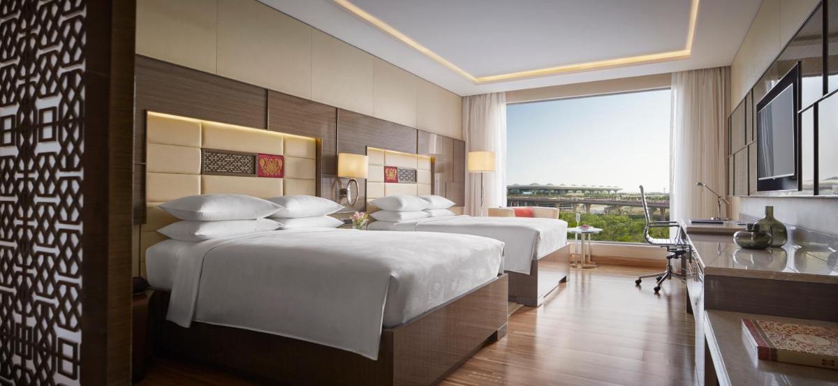 a hotel room with three beds and a window at JW Marriott Mumbai Sahar Airport in Mumbai a hotel room with three beds and a window at JW Marriott Mumbai Sahar Airport in Mumbai