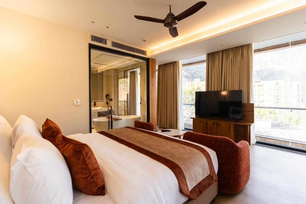 a bedroom with a large bed and a flat screen tv at Antalya By Divine Ganga Cottage in Rishīkesh