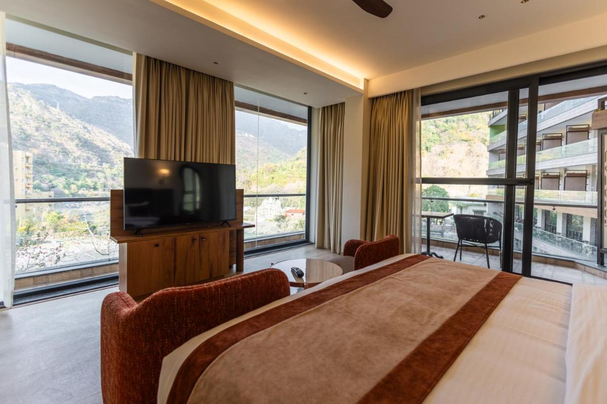 a bedroom with a large bed with a television and windows at Antalya By Divine Ganga Cottage in Rishīkesh