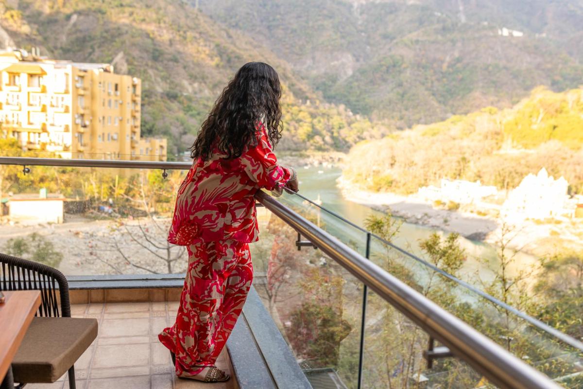 a woman standing on a balcony looking at a river at Antalya By Divine Ganga Cottage in Rishīkesh