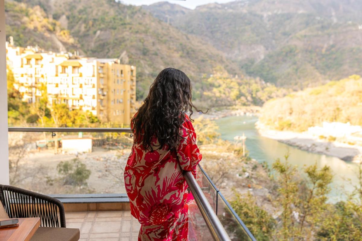 a woman standing on a balcony looking at a river at Antalya By Divine Ganga Cottage in Rishīkesh