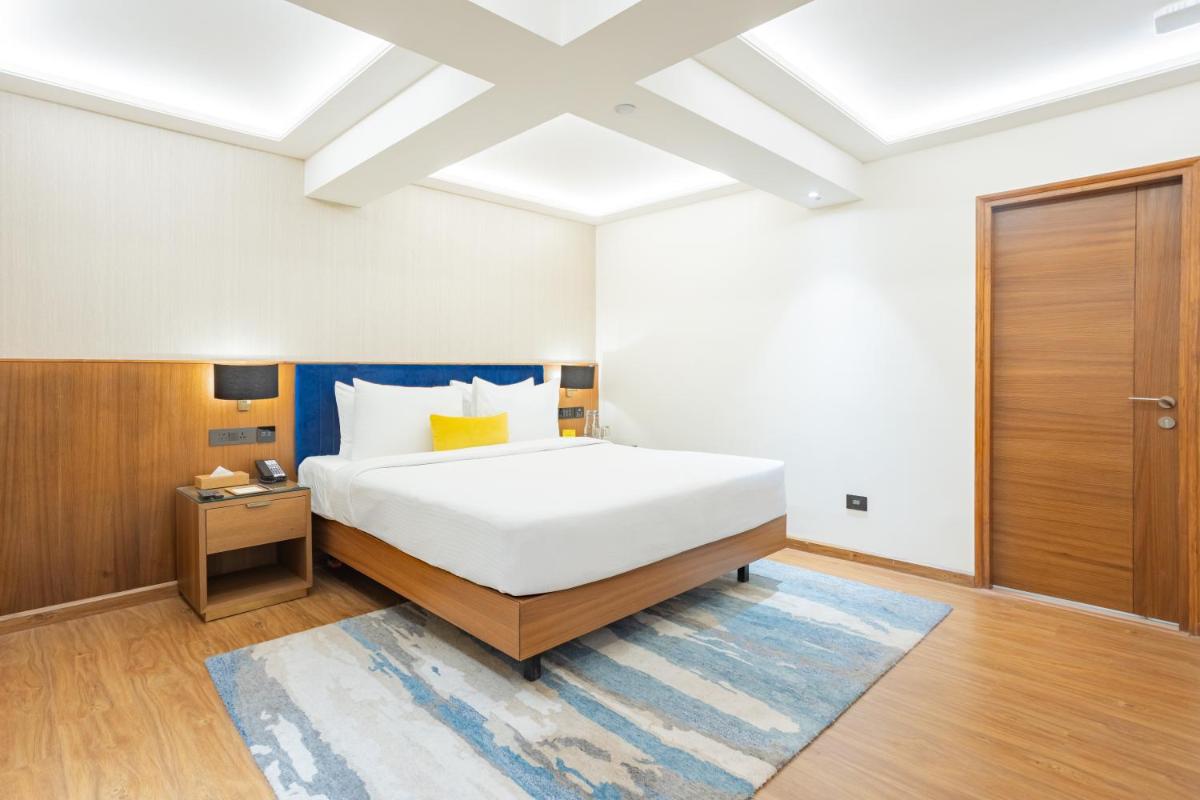 a bedroom with a large white bed and a wooden door at Golden Tulip Jaipur in Jaipur