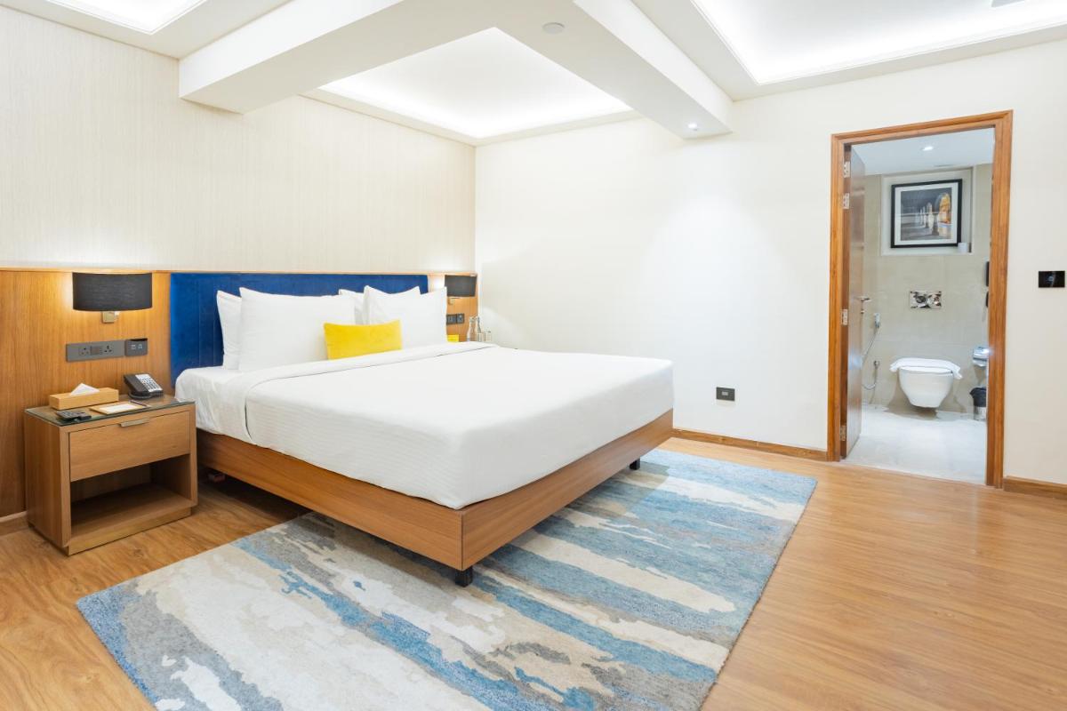 a bedroom with a large white bed and a bathroom at Golden Tulip Jaipur in Jaipur
