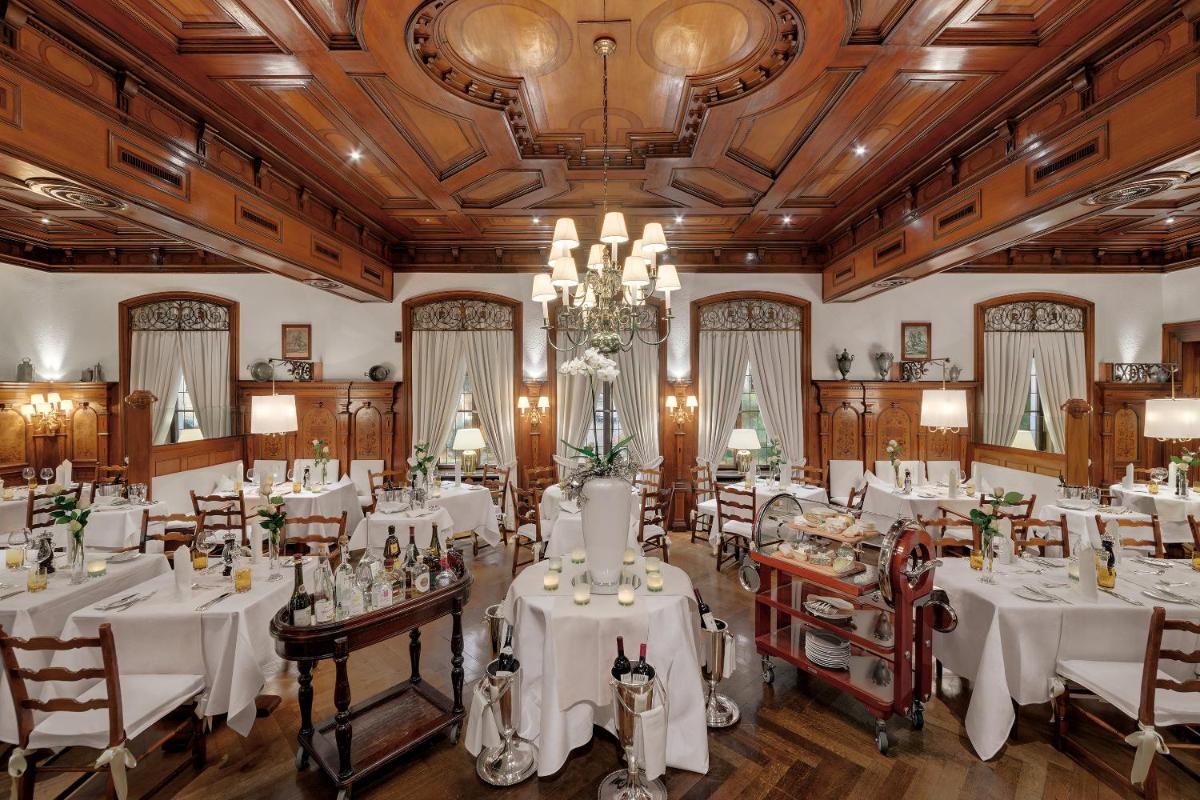 ein Esszimmer mit weißen Tischen und Stühlen und einem Kronleuchter in der Unterkunft Hotel Europäischer Hof Heidelberg, Bestes Hotel Deutschlands in historischer Architektur in Heidelberg