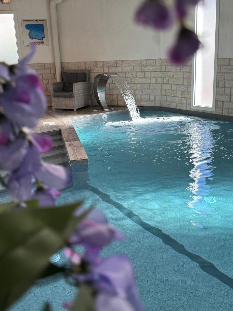 - une piscine avec une fontaine et des fleurs violettes dans l'établissement Hôtel Calme Des Pins & Spa, à Les Sables-dʼOlonne
