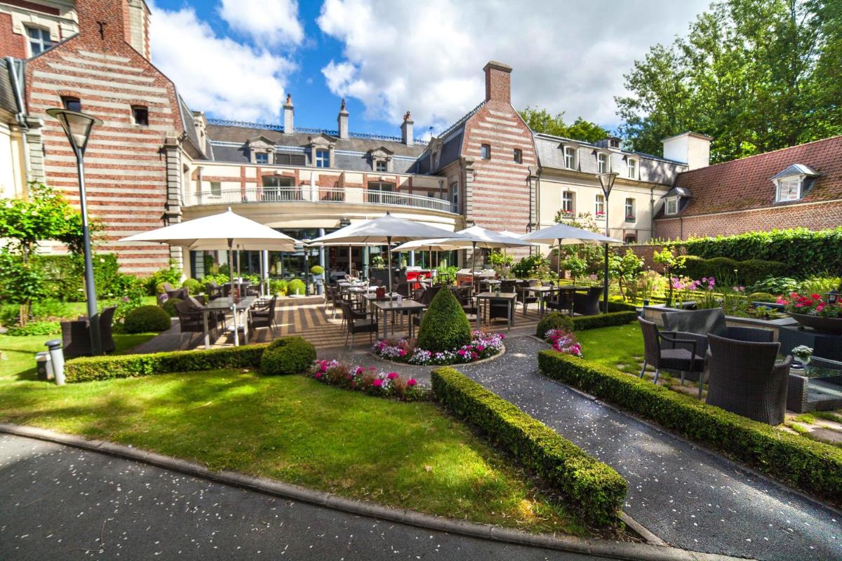 un jardin avec des tables et des parasols devant un bâtiment dans l'établissement Le Domaine de Beaulieu, à Busnes 124 autres photos