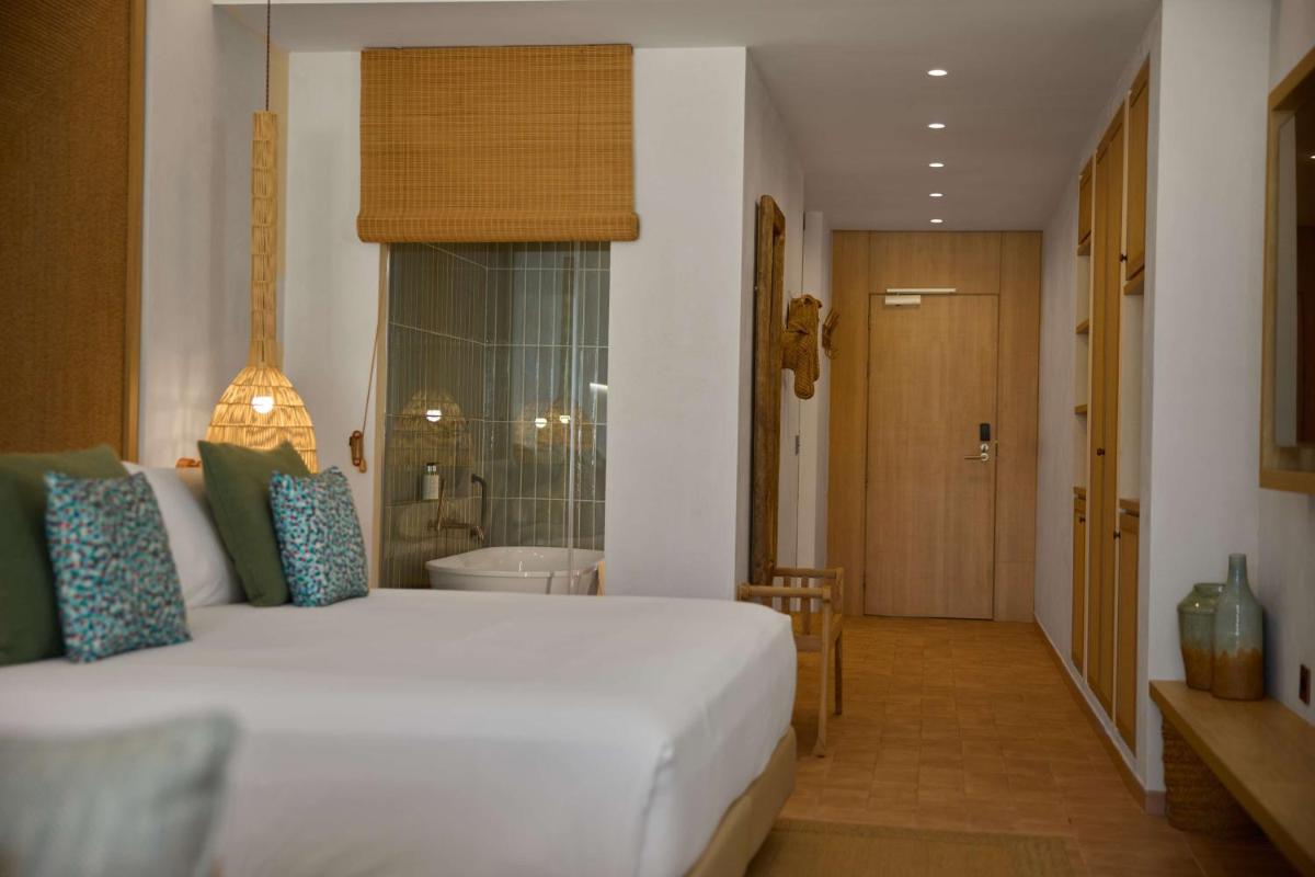 Un dormitorio con una gran cama blanca y un baño. en Cala San Miguel Ibiza Resort, Adults only, Curio Collection by Hilton, en Puerto de San Miguel