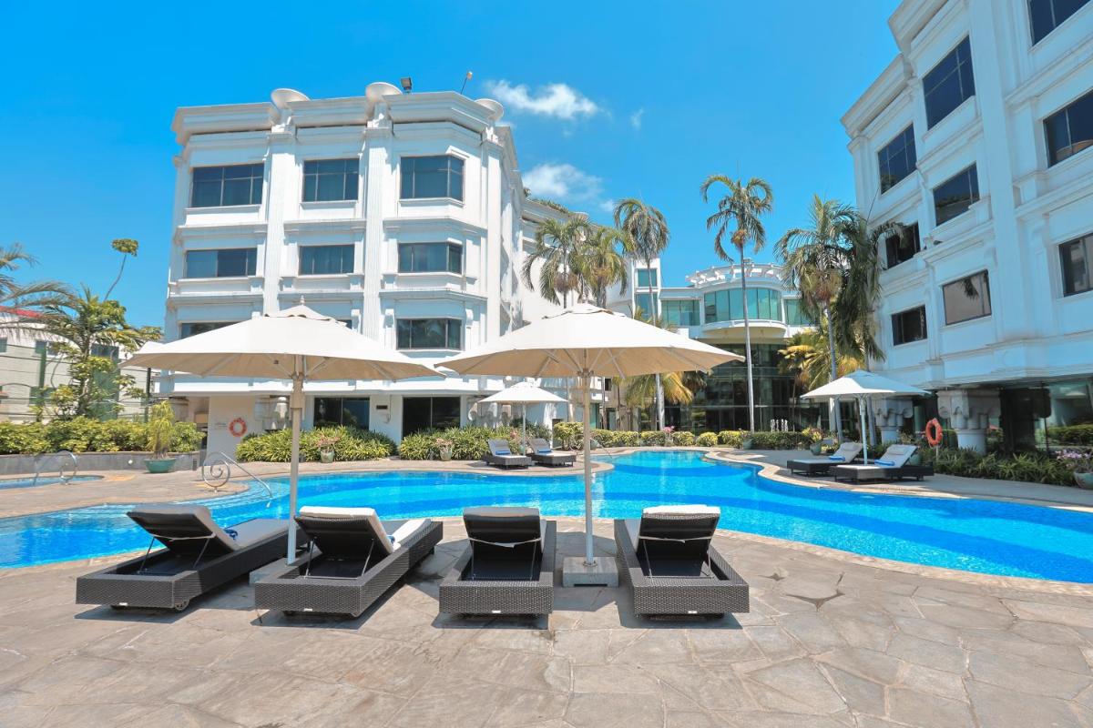 a pool with chairs and umbrellas next to a building at Le Royal Meridien Chennai in Chennai