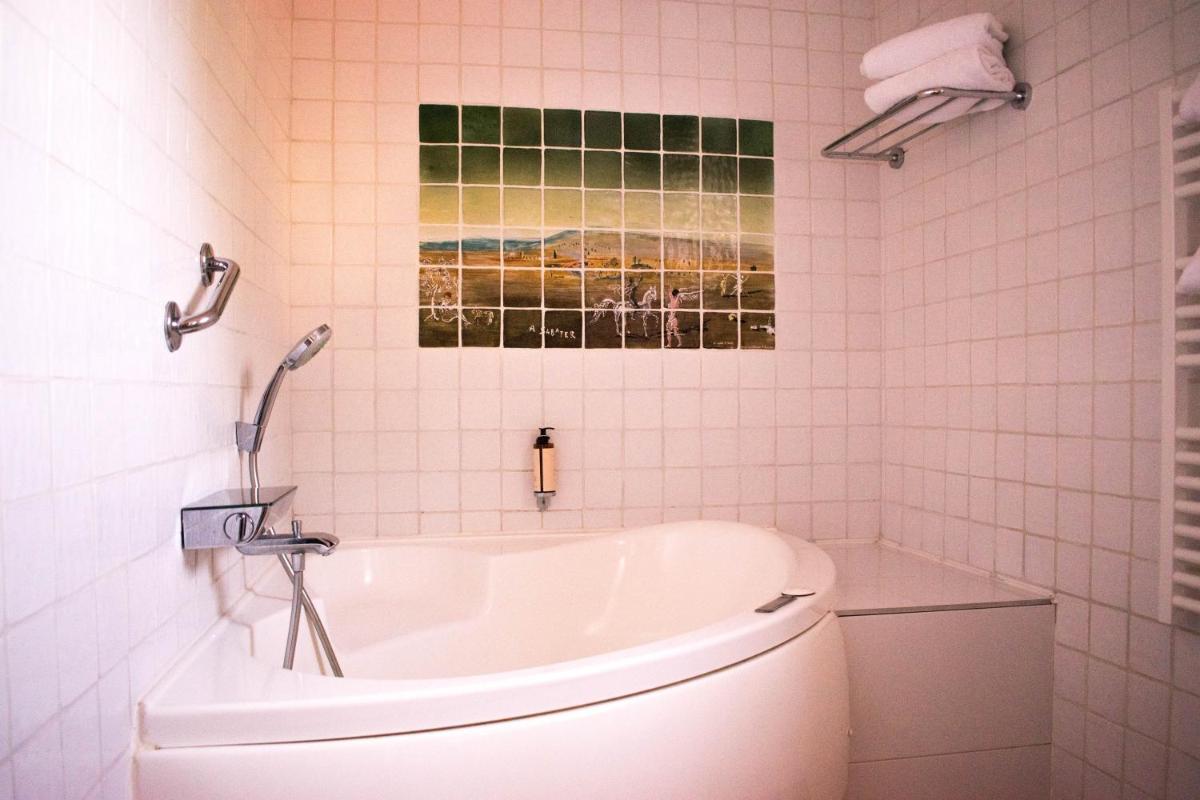 une salle de bains avec une baignoire blanche et un tableau accroché au mur dans l'établissement Le Relais Des Trois Mas, à Collioure