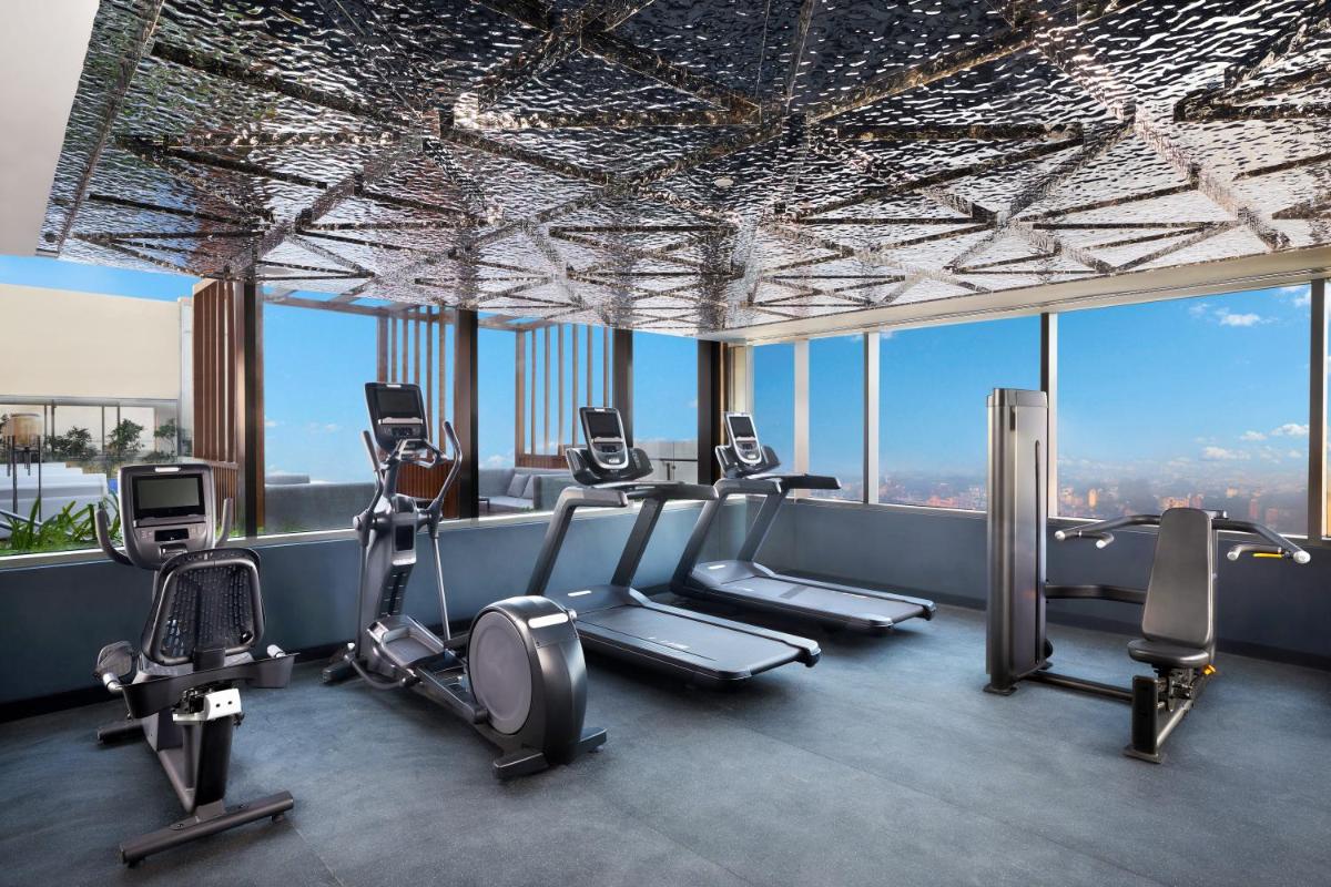 a gym with several tread machines in a building with windows at Novotel New Delhi City Centre in New Delhi a gym with several tread machines in a building with windows at Novotel New Delhi City Centre in New Delhi