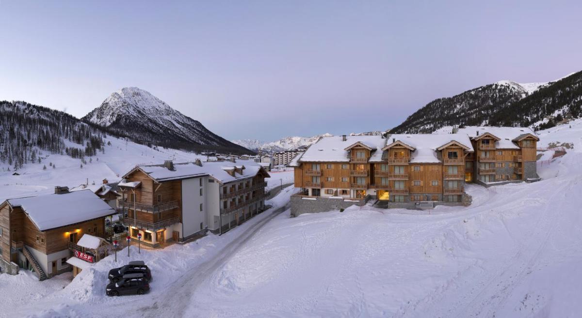 un groupe de bâtiments dans la neige à côté d'une montagne dans l'établissement CGH Résidence Boutique Le Chalet des Dolines, à Montgenèvre