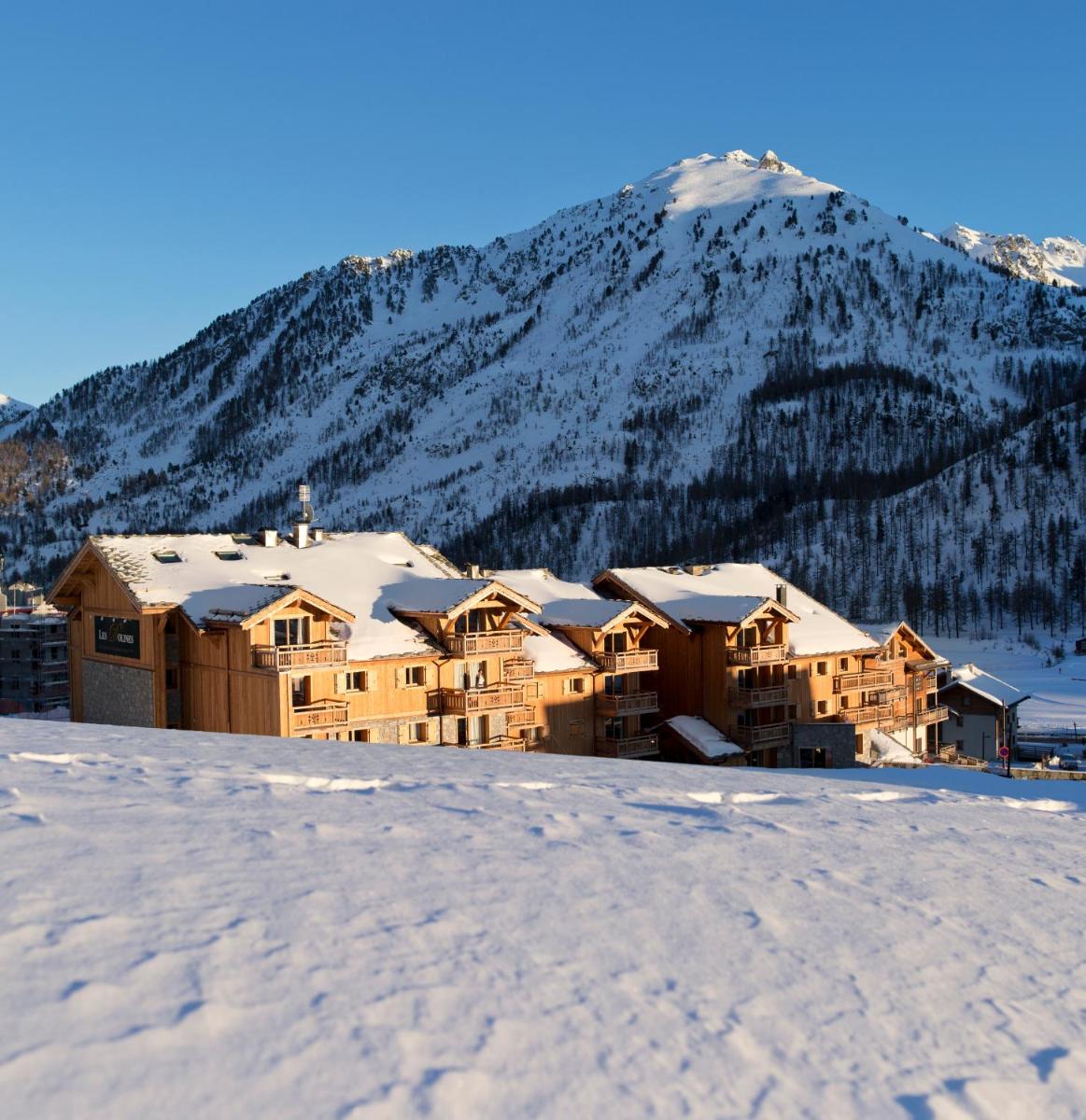 un lodge dans la neige avec une montagne en arrière-plan dans l'établissement CGH Résidence Boutique Le Chalet des Dolines, à Montgenèvre
