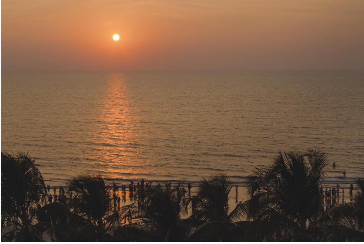 a sunset over the ocean with palm trees in the foreground at Ramada Plaza By Wyndham Palm Grove in Mumbai