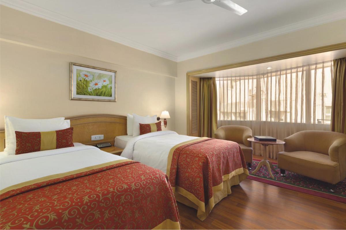 a hotel room with two beds and a chair and a window at Ramada Plaza By Wyndham Palm Grove in Mumbai