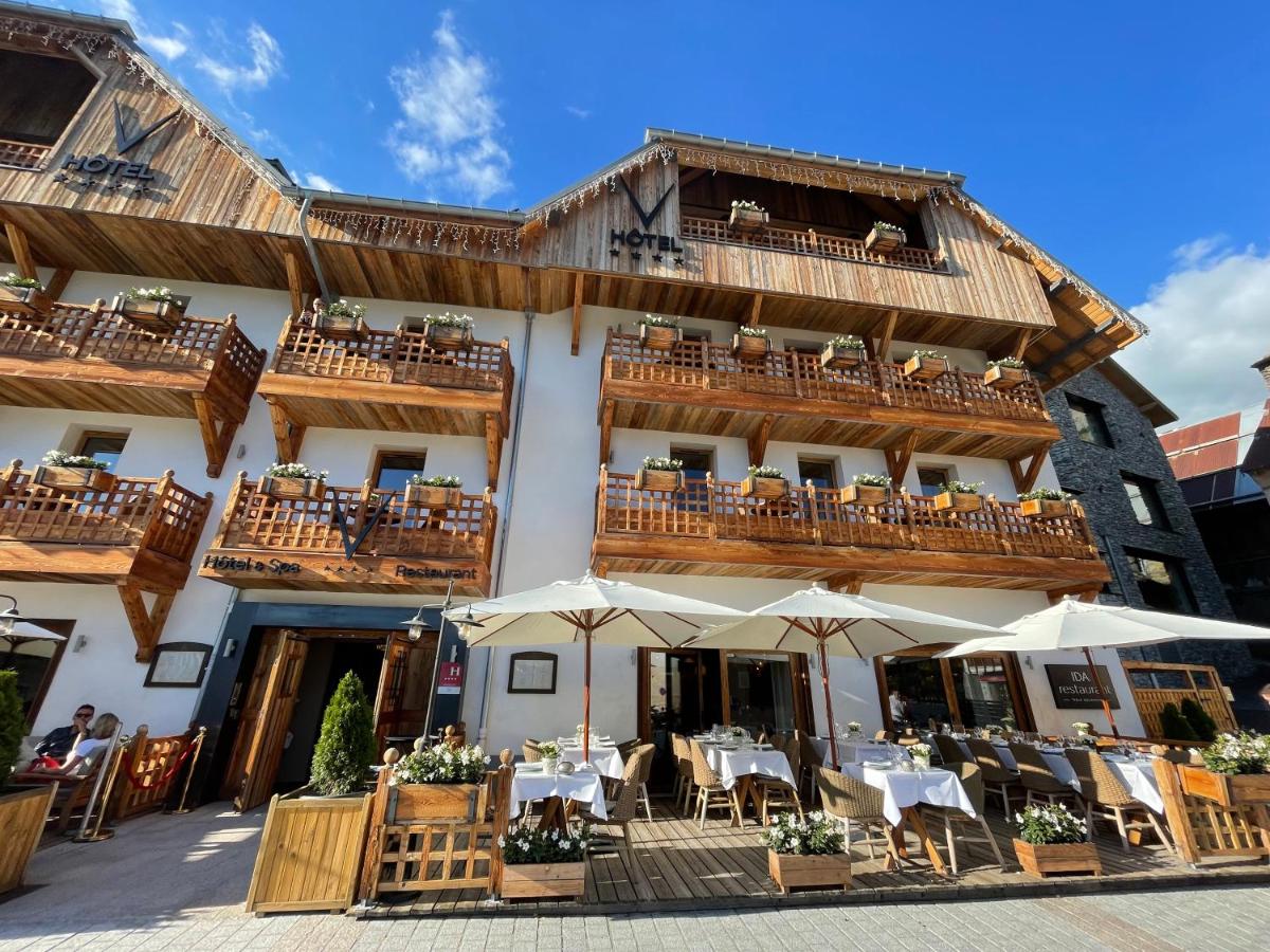 un bâtiment avec des tables et des parasols devant lui dans l'établissement Hotel Le V de Vaujany, à Vaujany