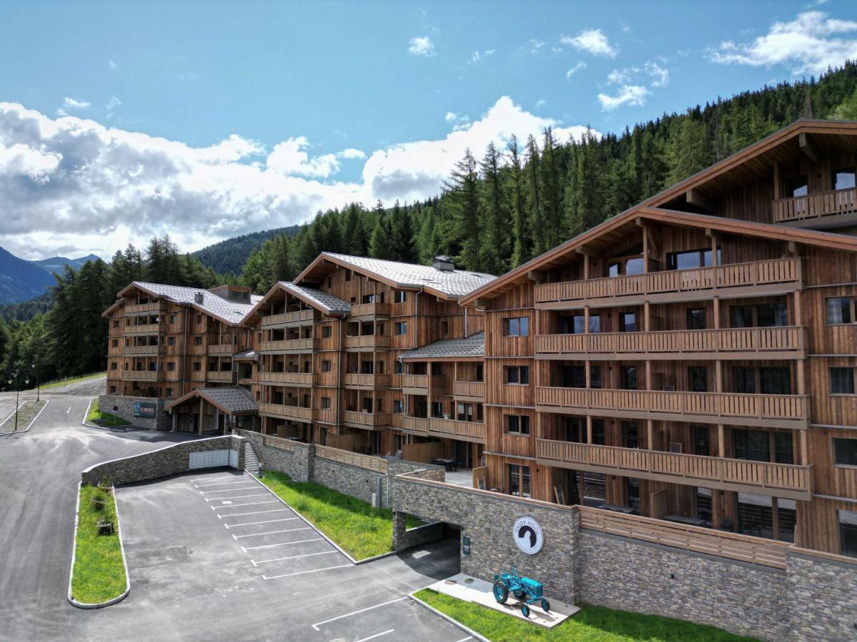 un immeuble dans les montagnes avec un parking dans l'établissement TERRESENS - Le Snoroc, à Aime La Plagne