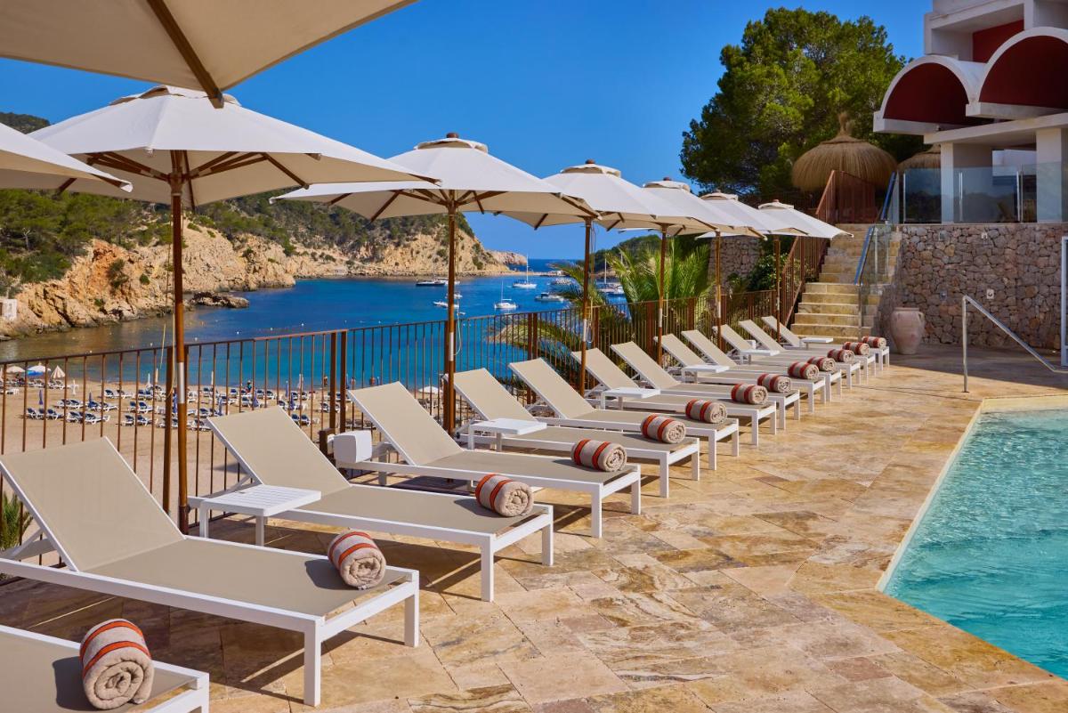 una fila de tumbonas con sombrillas junto a una piscina en Cala San Miguel Ibiza Resort, Adults only, Curio Collection by Hilton, en Puerto de San Miguel