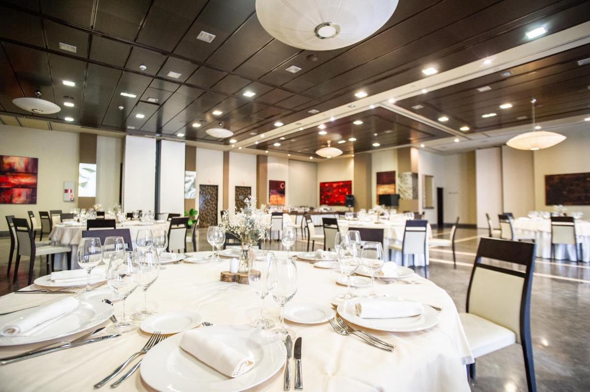 Un gran comedor con mesas y sillas blancas. en AZZ Asturias LangreHotel & Spa, en Langreo