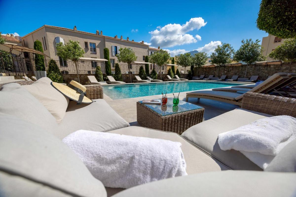 une piscine avec des chaises longues blanches et une piscine dans l'établissement Hôtel L'Abbaye, à Calvi