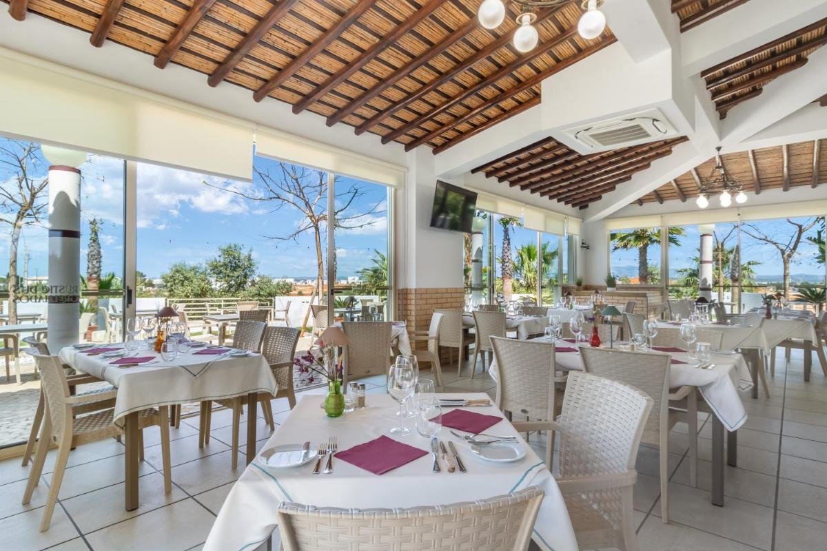 um restaurante com mesas e cadeiras brancas e grandes janelas em Hotel Rural Brícia Du Mar em Ferragudo