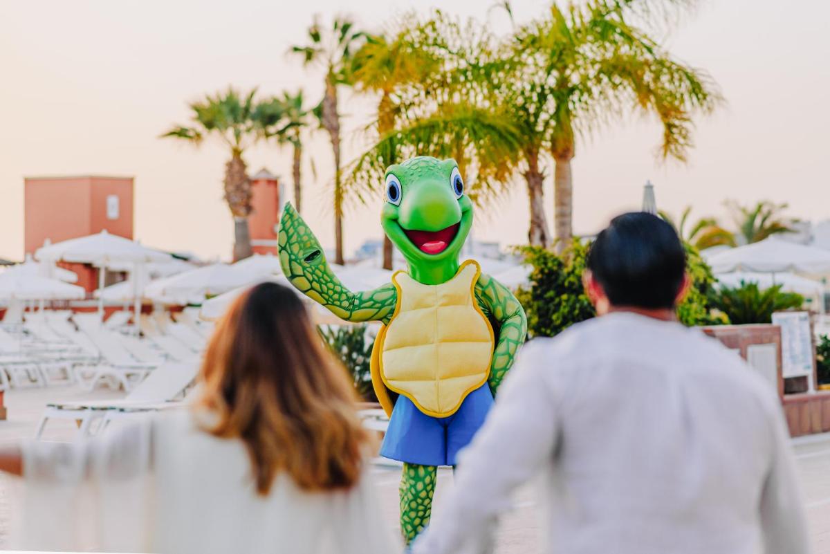 Un grupo de personas pasando junto a una mascota rana. en Landmar Costa los Gigantes Family Resort, en Puerto de Santiago
