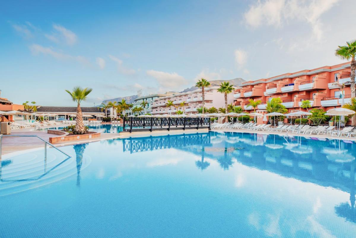 Una gran piscina con palmeras y edificios. en Landmar Costa los Gigantes Family Resort, en Puerto de Santiago