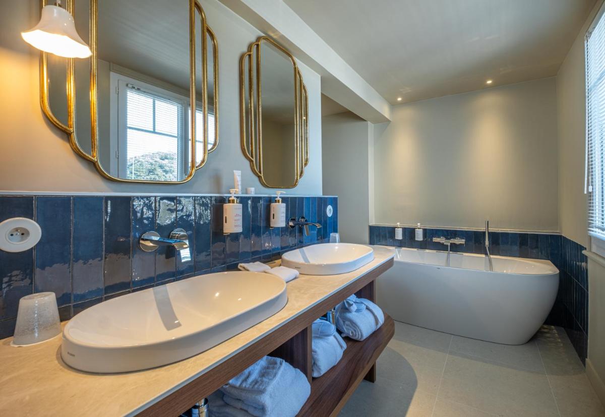 La salle de bains est pourvue de 2 lavabos, d'une baignoire et de miroirs. dans l'établissement Hôtel de la Plage, à Plonévez-Porzay