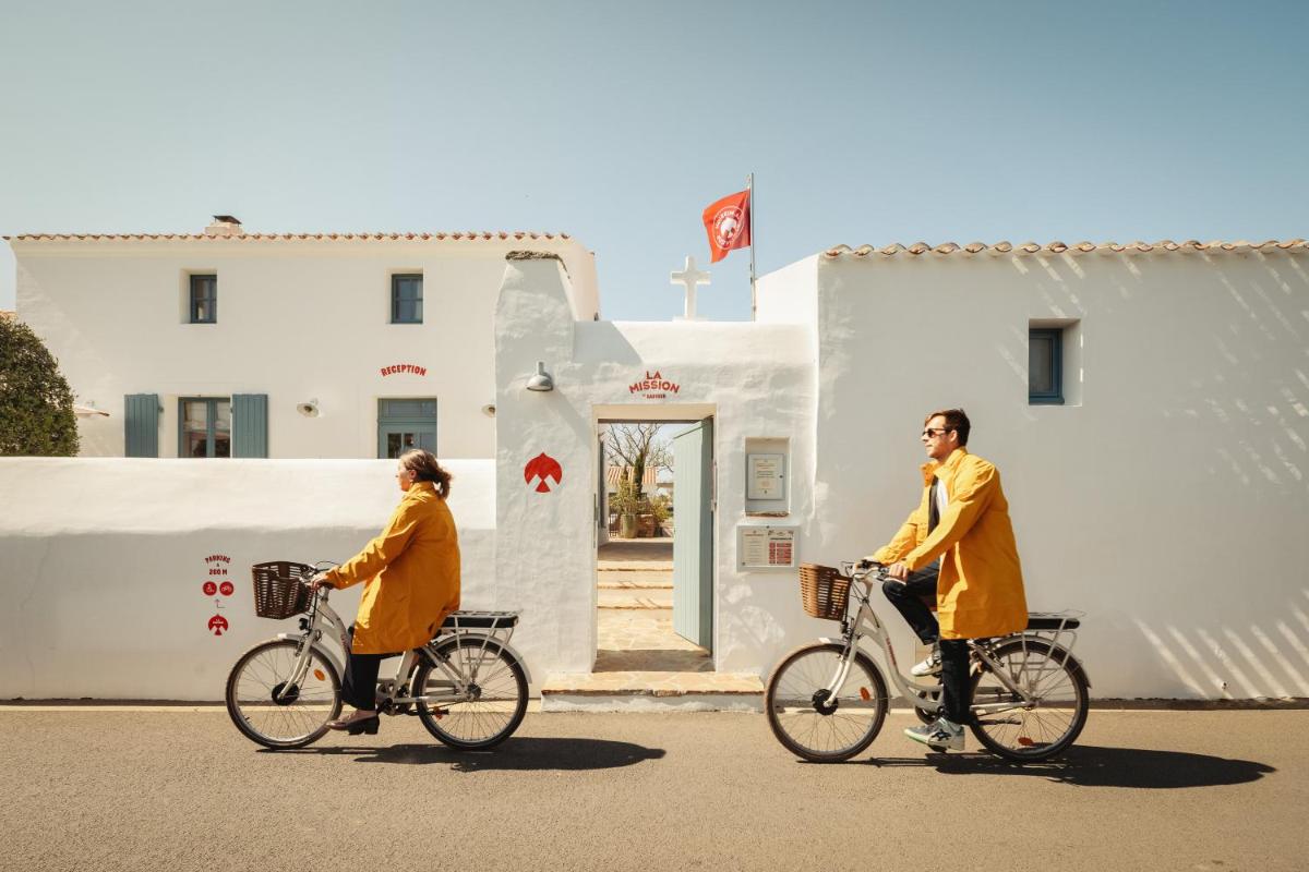 deux femmes en manteaux faisant du vélo dans une rue dans l'établissement La Mission Hôtel & SPA - l'île d'Yeu, à L'Ile d'Yeu