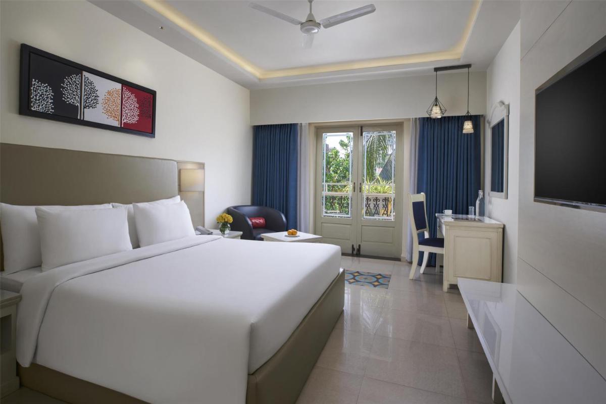 a bedroom with a large white bed and a desk at Radisson Goa Candolim in Candolim
