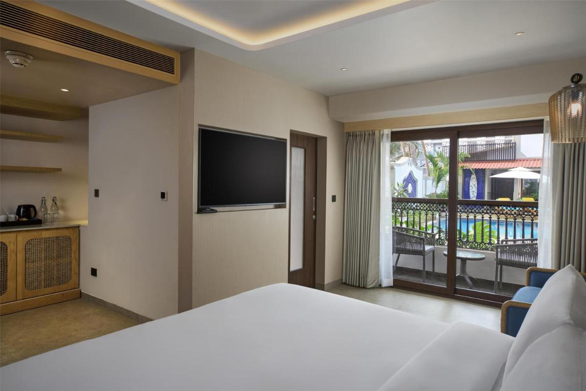 a bedroom with a bed and a television and a balcony at Radisson Goa Candolim in Candolim