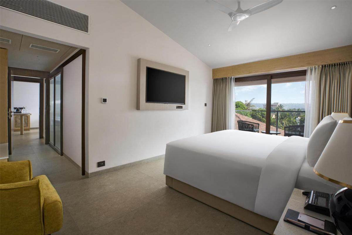 a white bedroom with a large bed and a tv at Radisson Goa Candolim in Candolim