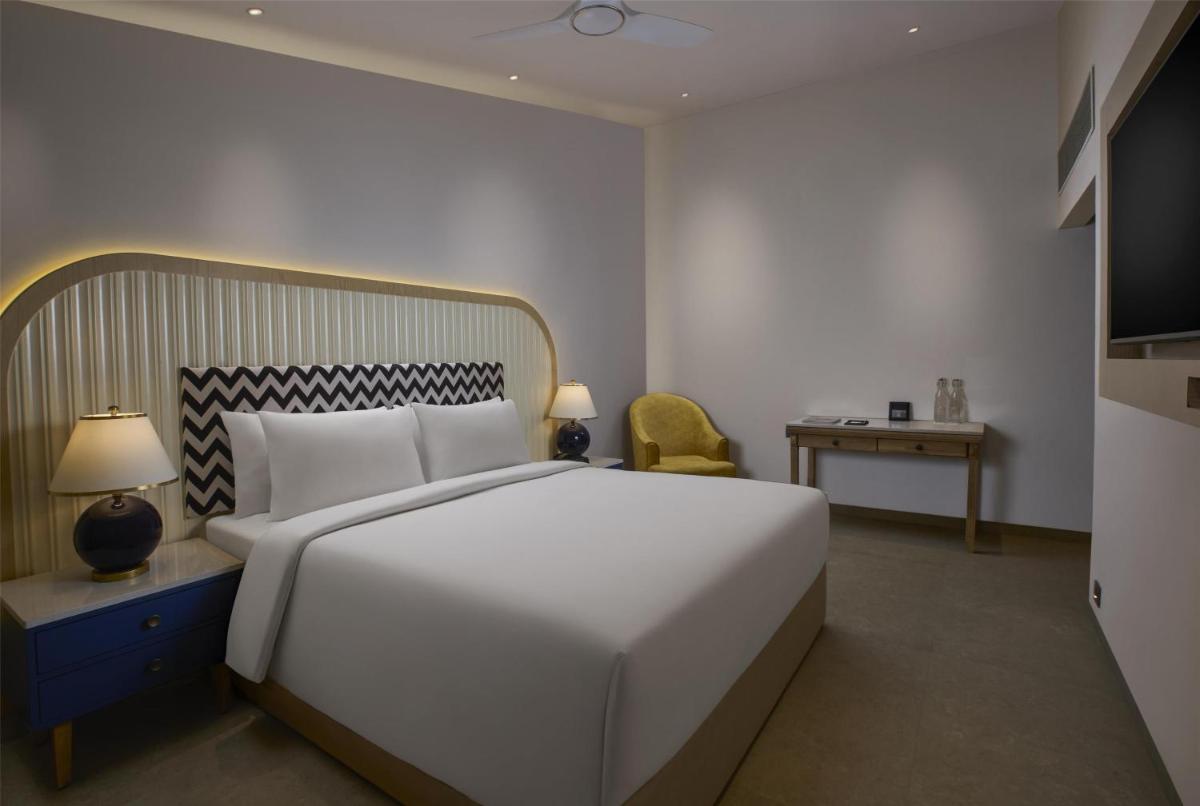 a bedroom with a large white bed and a chair at Radisson Goa Candolim in Candolim